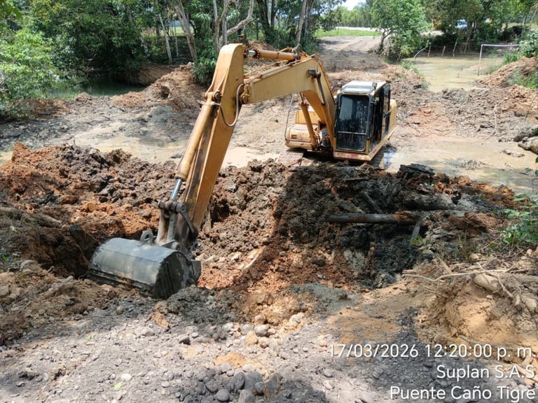 Two excavators working on a dirt construction site with pile of soil and green trees in background