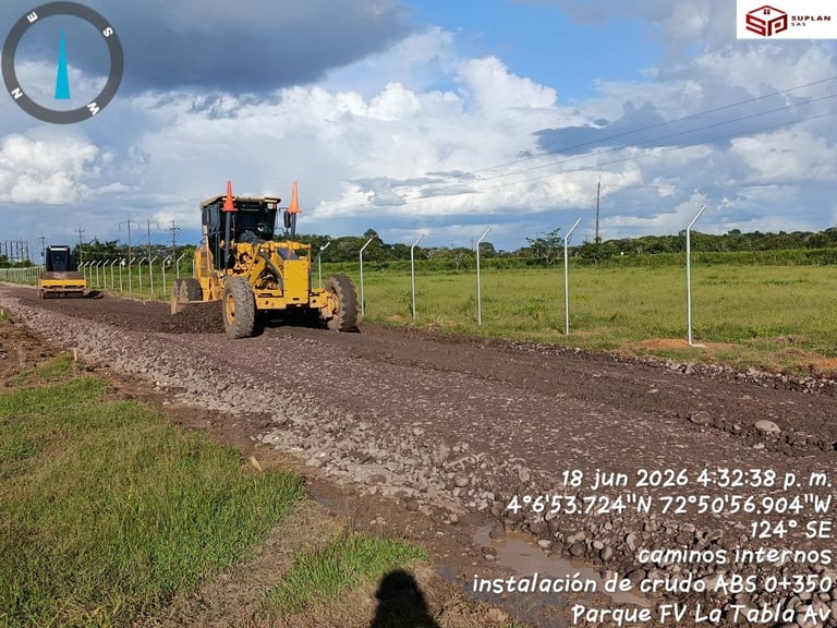 Yellow grader machine leveling rural road with fencing and green fields under cloudy sky