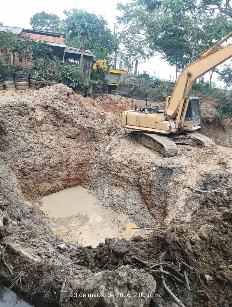 Excavator working in muddy construction site with piles of earth and machinery visible amid trees