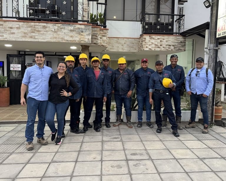 Group of construction workers standing in front of a brick building, most wearing yellow hard hats and safety gear