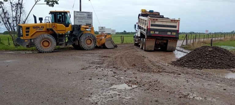 Yellow front-end loader and dump truck distributing mulch or gravel on a rural road under cloudy sky